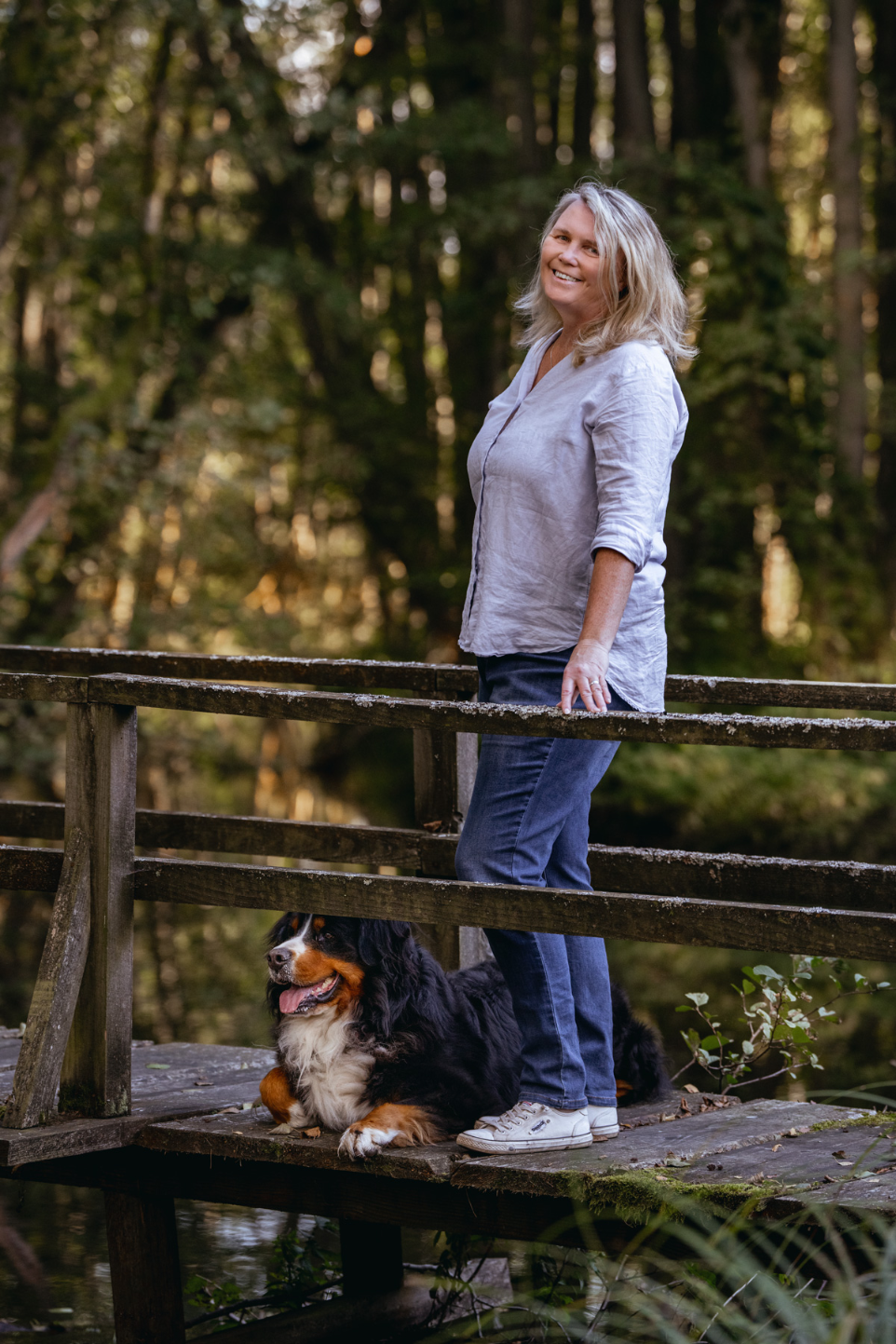 Elke Junghans | Gründerin von NEUSTART finden steht mit ihrem Hund auf einem Holzsteg in ruhiger Waldumgebung
